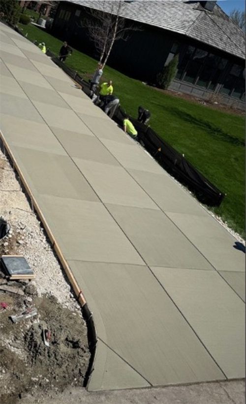 Construction workers laying concrete sidewalk. Grassy slope to right.