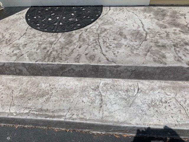 Concrete steps leading to a doorway, with a decorative black mat on the top step.