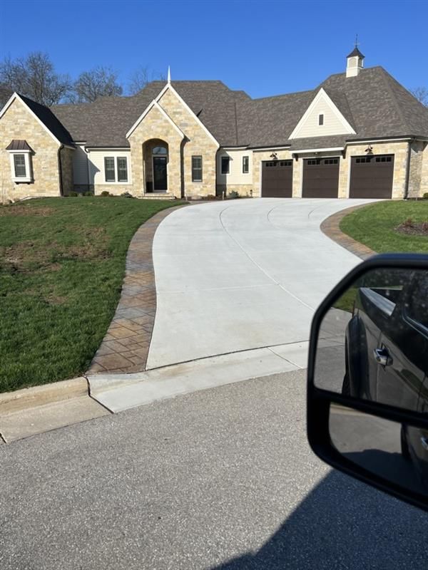 Stone and tan house with brown garage doors and a curved concrete driveway.