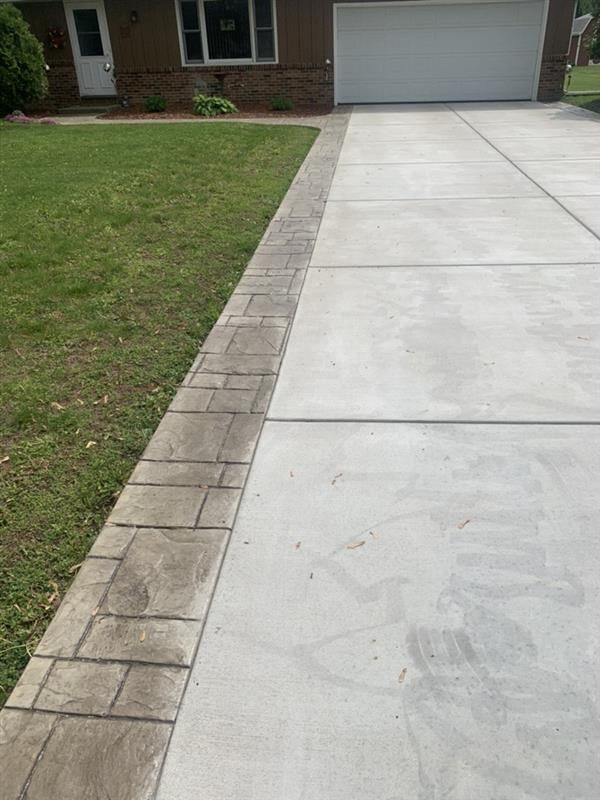 Concrete driveway with stamped border next to a grassy lawn.