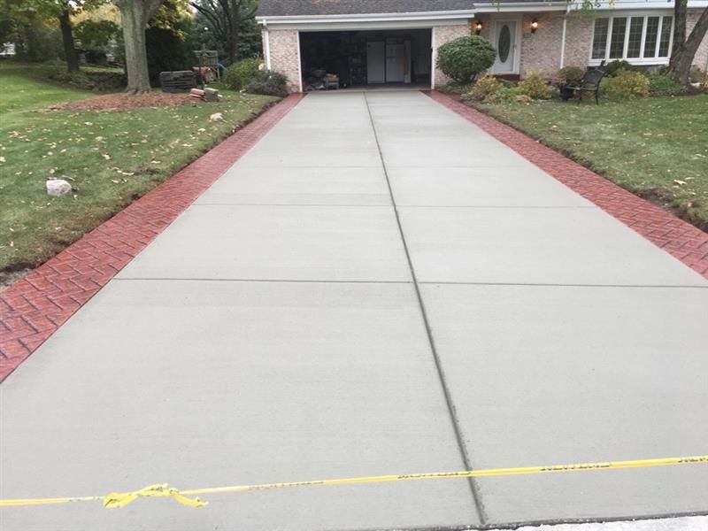 Driveway with brick borders, leading to a garage. Concrete surface, green grass on sides.