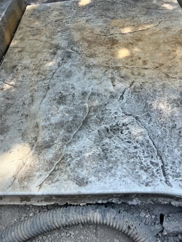 Stamped concrete patio with large cracks, shades of gray and tan. A corrugated pipe is at the bottom.