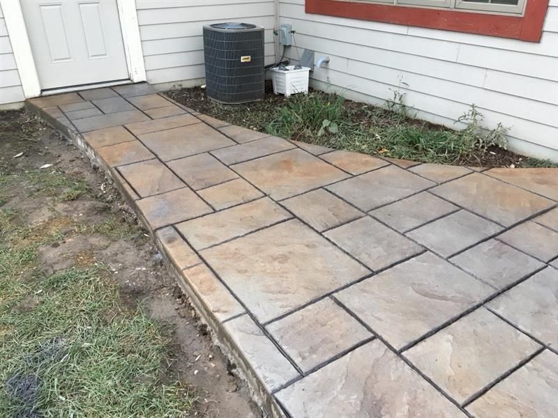 Stone paver walkway leading to a white door next to a house with an AC unit.