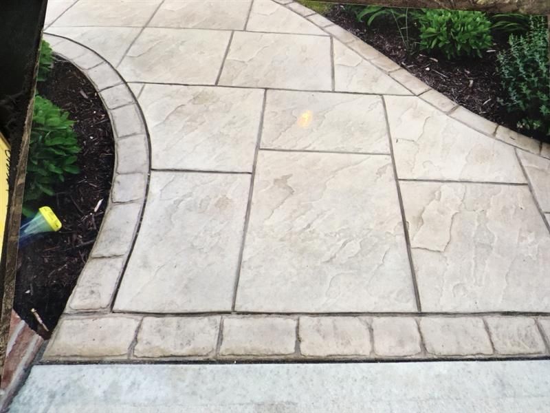 Stone pathway with curved edges and rectangular patterns, bordered by a dark mulch bed.