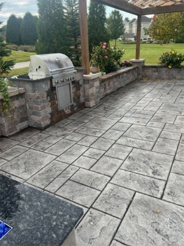 Outdoor patio with built-in grill, stone retaining wall, and patterned concrete pavers.