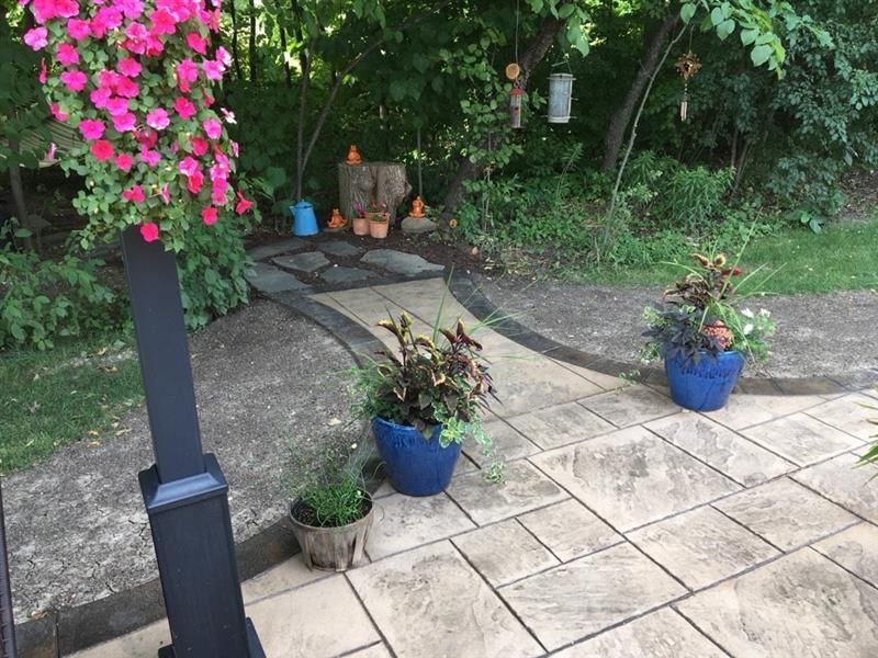 Stone path with blue planters, pink flowers, and lush green foliage.