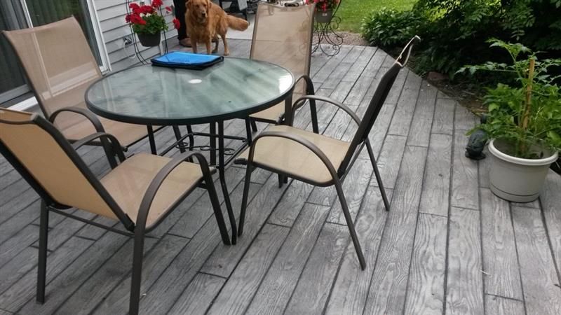 Outdoor patio set on a weathered wooden deck with a dog in the background.