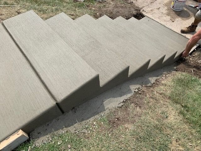 Newly poured concrete steps leading from a grassy area to a walkway.