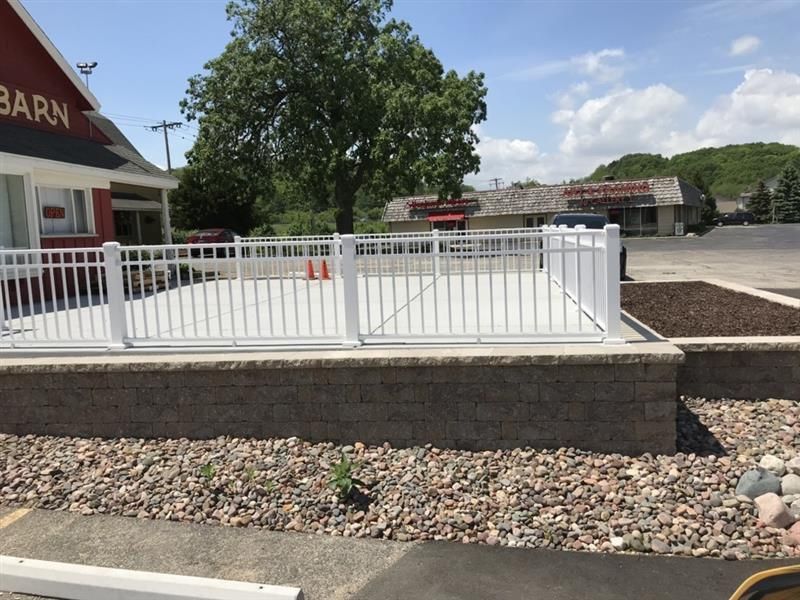 White-railed deck atop a brick wall with rocks in front, beside a red building with the sign 