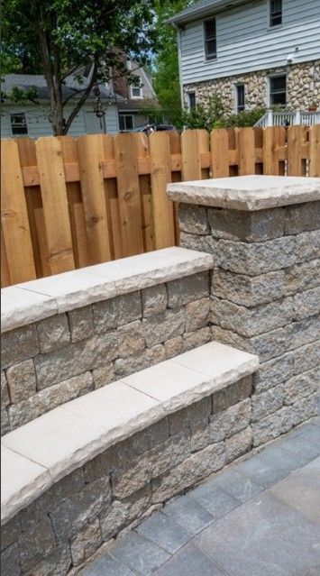 Stone steps leading up to a wooden fence, outdoors. Beige and brown tones.