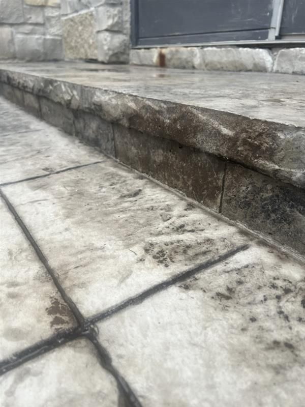 Stone textured concrete steps leading to a doorway, with darker grout lines.