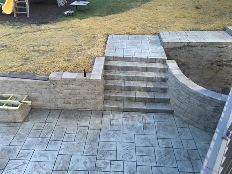 Concrete patio with steps, retaining walls, and a lawn.