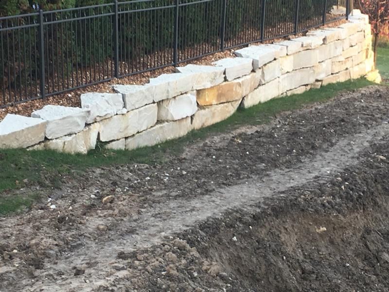 Stone retaining wall with a black fence above, dirt slope in foreground.
