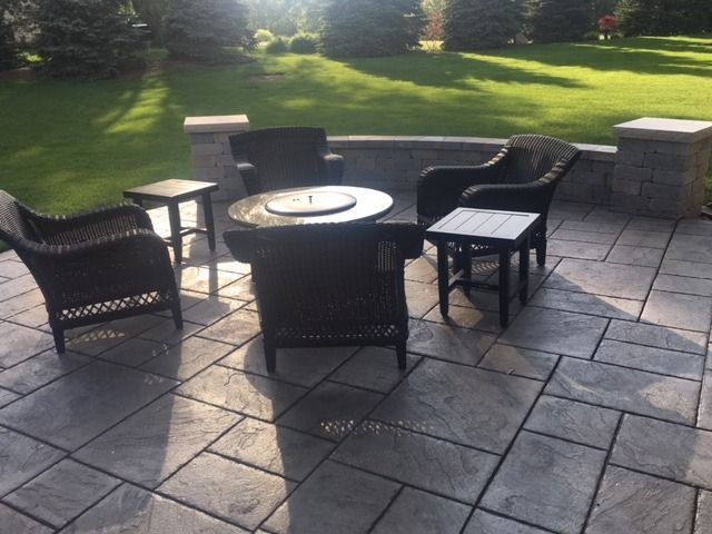 Patio with dark wicker furniture, fire pit table, and stone pavers, with a grassy lawn in the background.