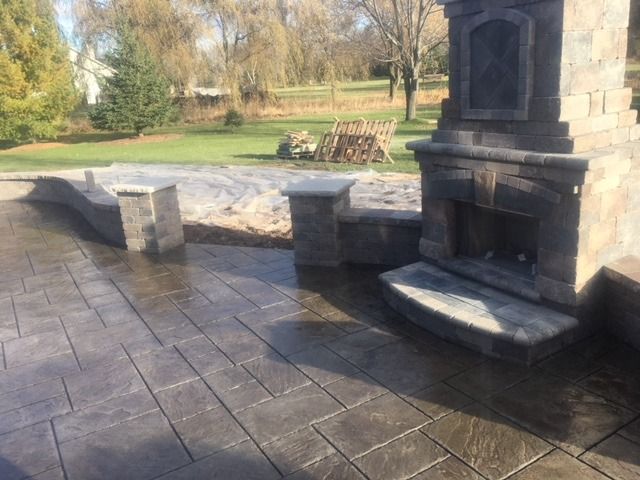 Stone patio with outdoor fireplace and built-in seating, in a backyard setting.