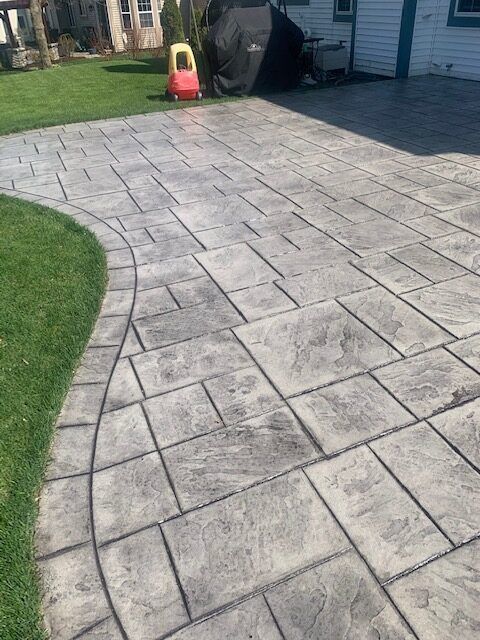 Stamped concrete patio with a curved walkway, gray stone-like pattern, next to a grassy lawn.