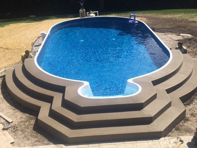 Oval-shaped swimming pool with concrete steps. Brown steps surround the blue water.