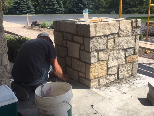 A person applies mortar to stone on a square column outdoors.