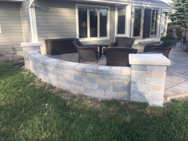 Outdoor patio with a curved stone retaining wall and wicker furniture.