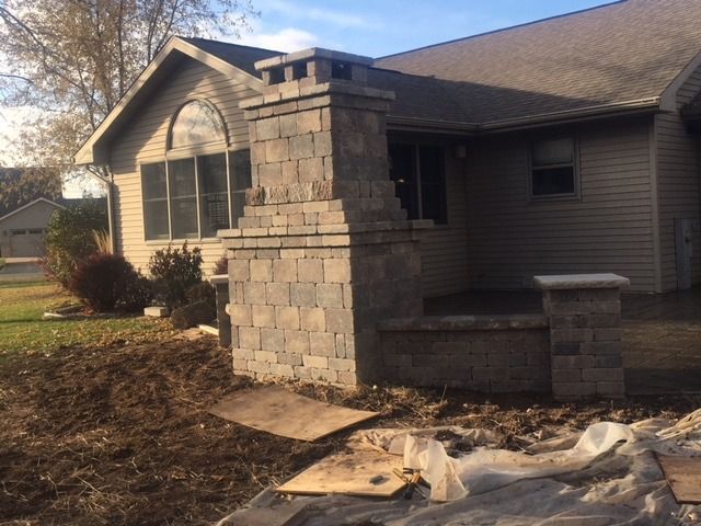 Stone chimney and porch under construction at a house. Dirt, wood, and materials are visible.
