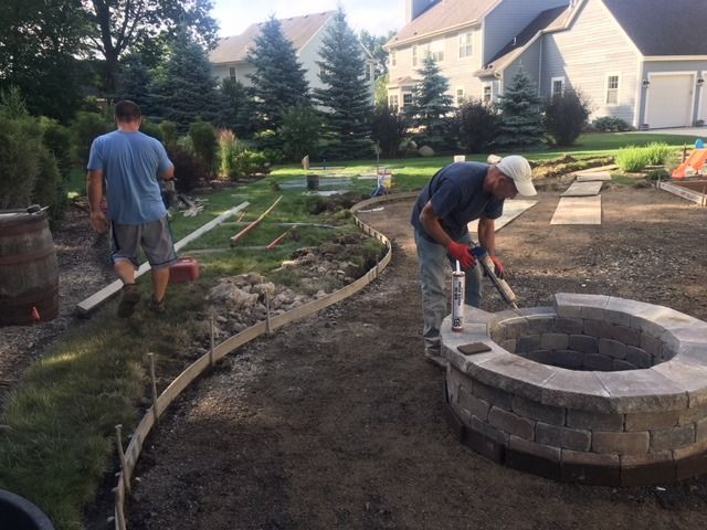 Two men building a stone fire pit and a curved pathway in a backyard.