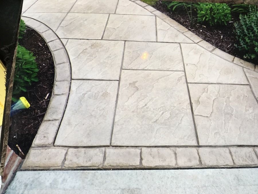 Concrete patio with curved border, rectangular and square sections, landscaped with plants.