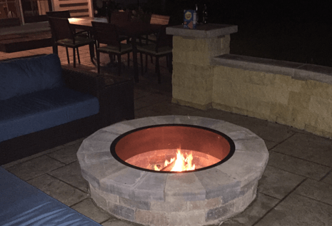 Fire pit with flames on a patio with outdoor furniture at night.
