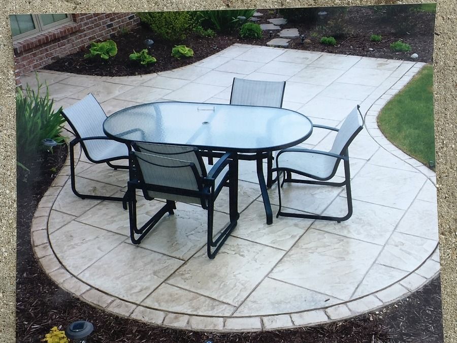 Patio with glass table and chairs, bordered by brick and landscaping.