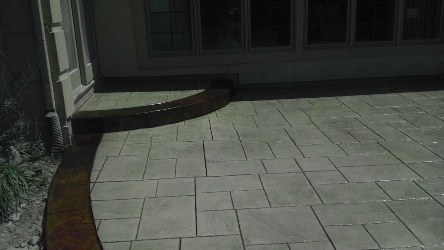 A concrete patio with a curved border next to a building's wall and windows.