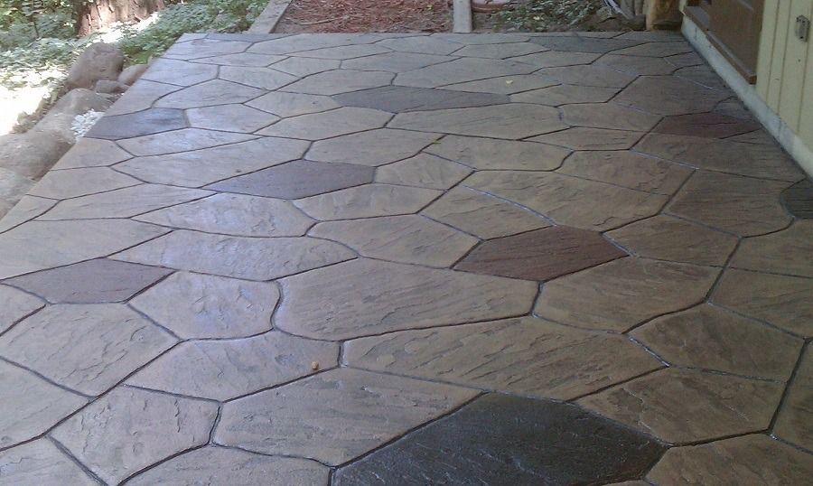 Stone-patterned concrete patio. Various shades of gray, brown, and reddish-brown. The patio sits next to a building.