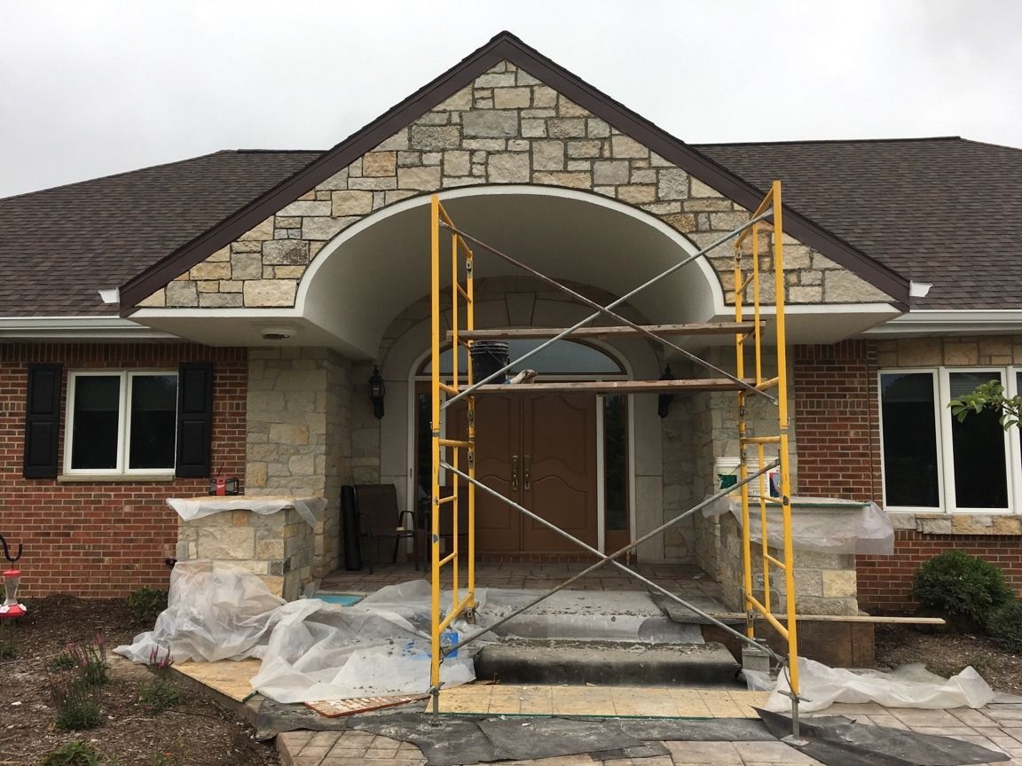 House exterior with stone and brick facade, arched entryway, scaffolding.