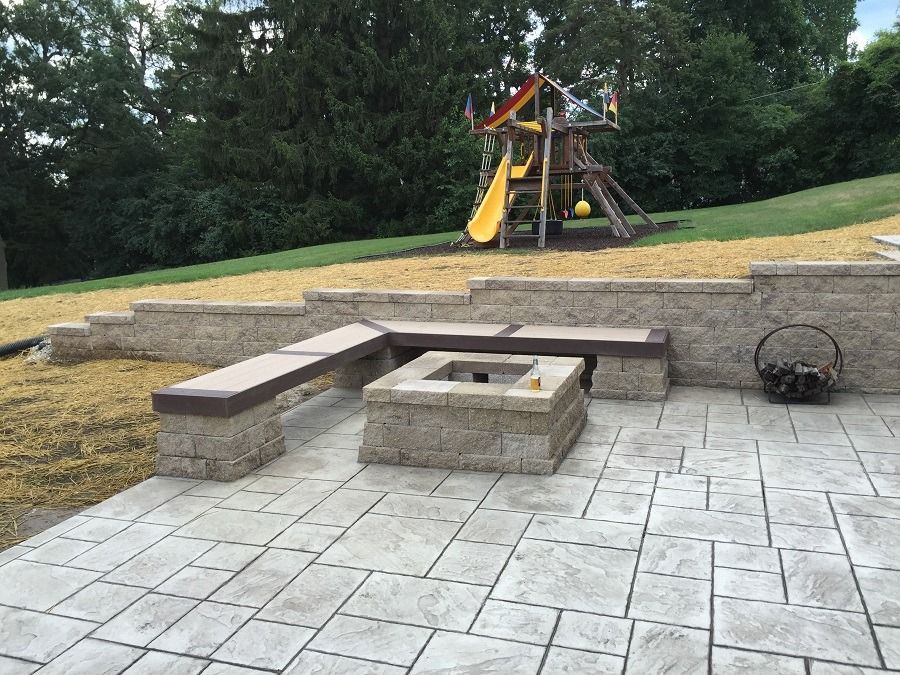Patio with fire pit, built-in benches, and playground on a grassy hill in the background.