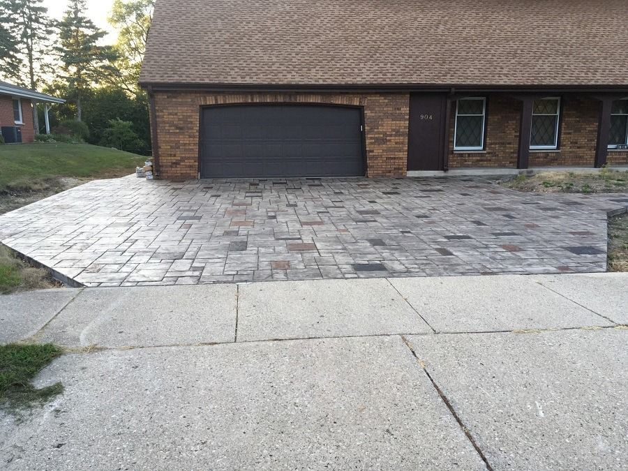 Brick paver driveway leading to a brick building with a garage door and sidewalk.