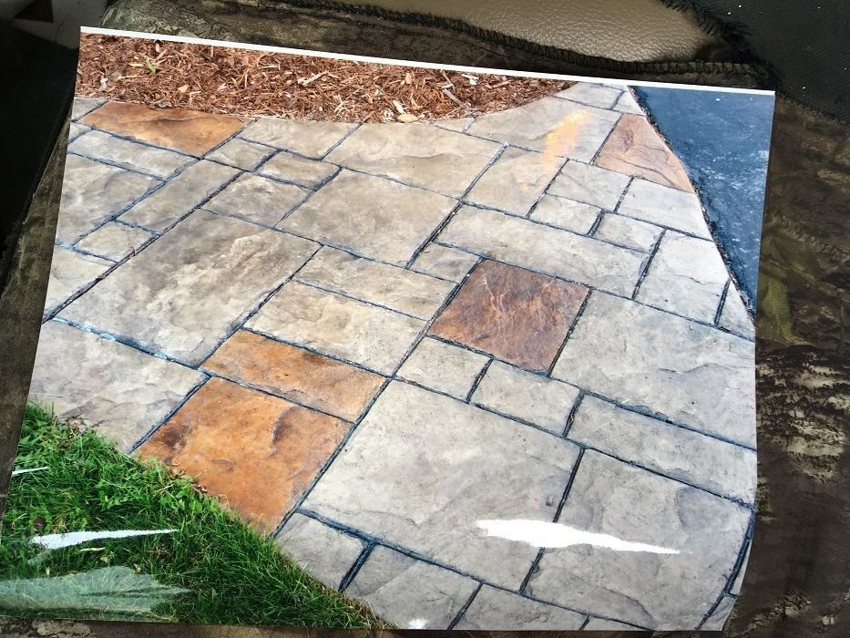 Stained concrete walkway with brown and gray tiles, next to grass and mulch.