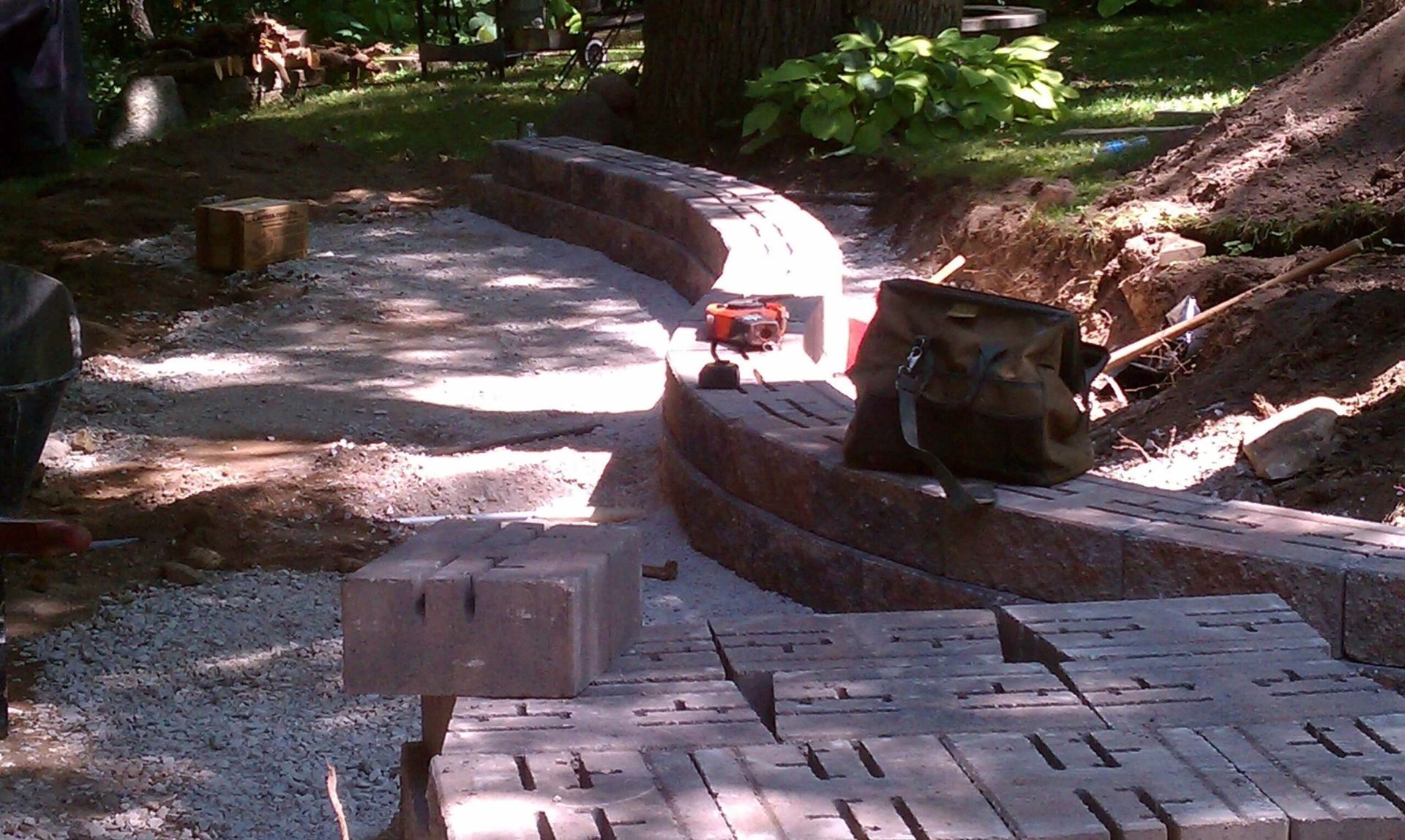 Stone retaining wall construction in a yard. Bricks, gravel, and tools are visible.