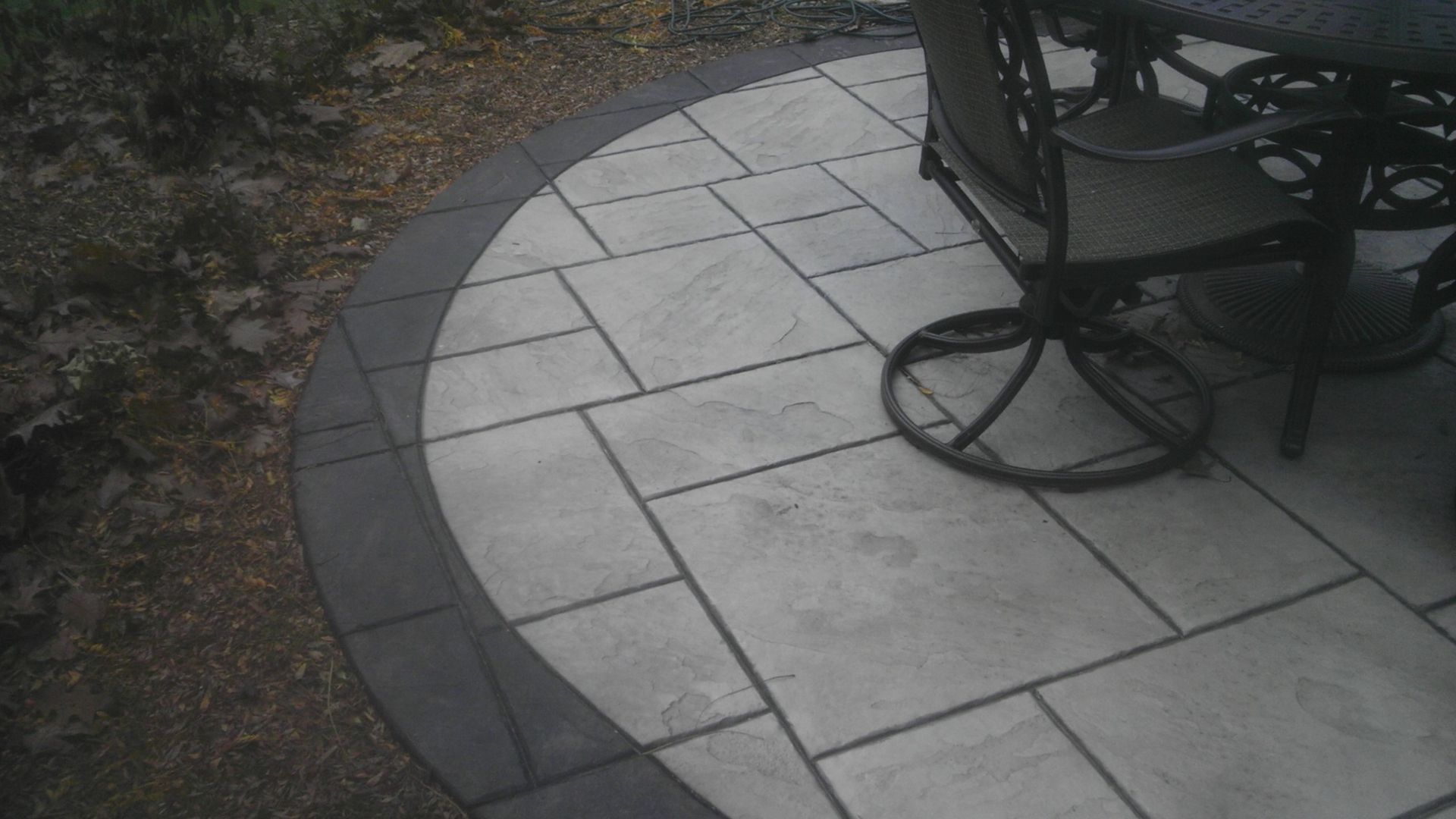 Circular stone patio with black border and patio furniture.