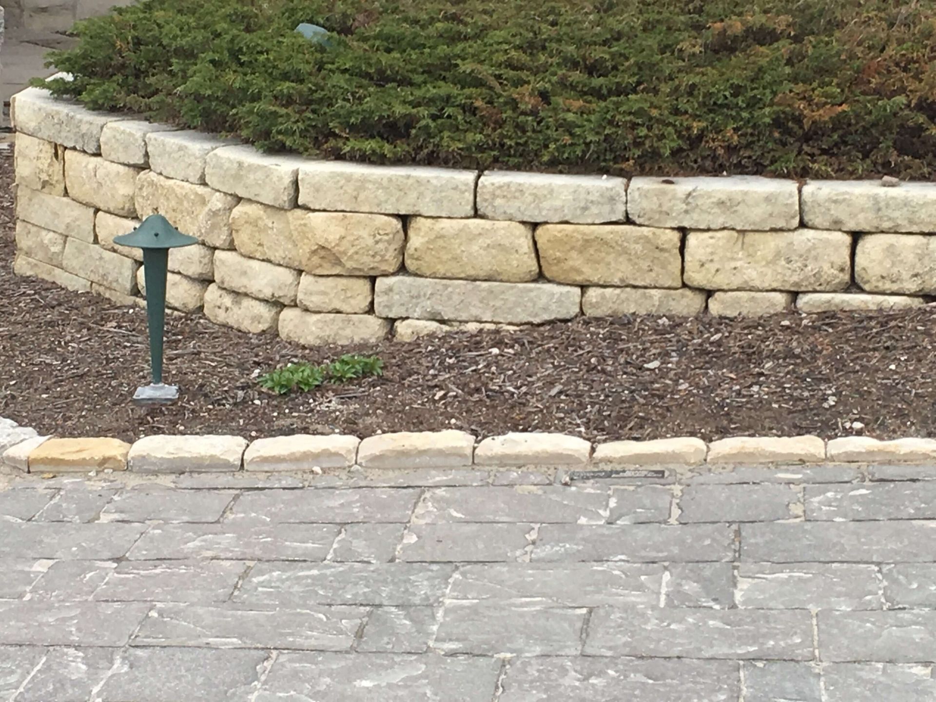 Stone retaining wall with a bed of greenery and a paved walkway.