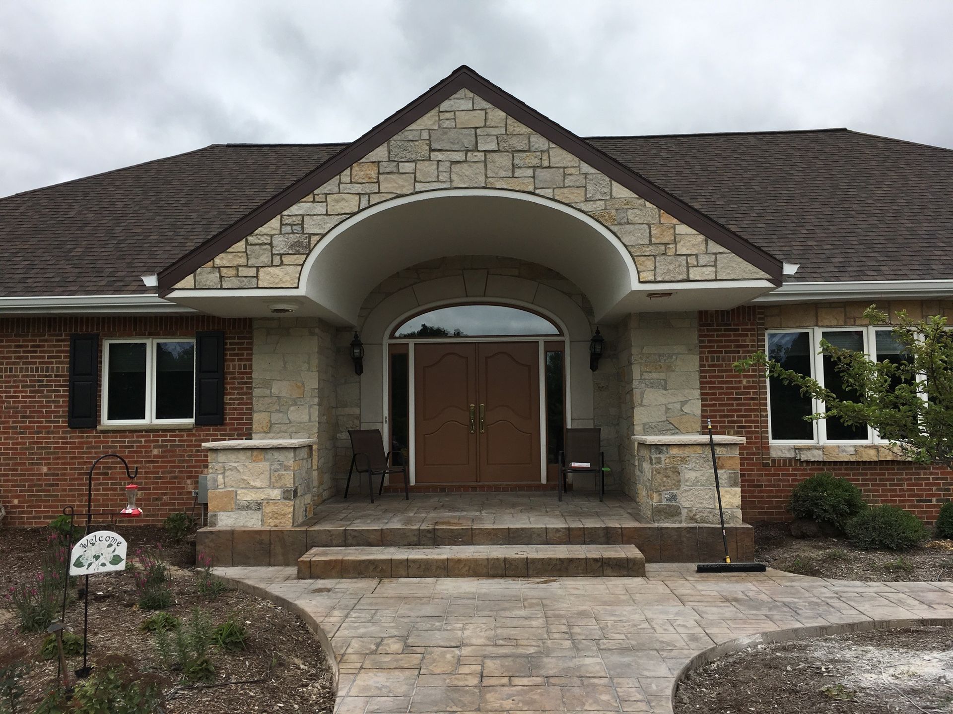 Brick house entrance with stone arch, double doors, steps, and paved walkway.