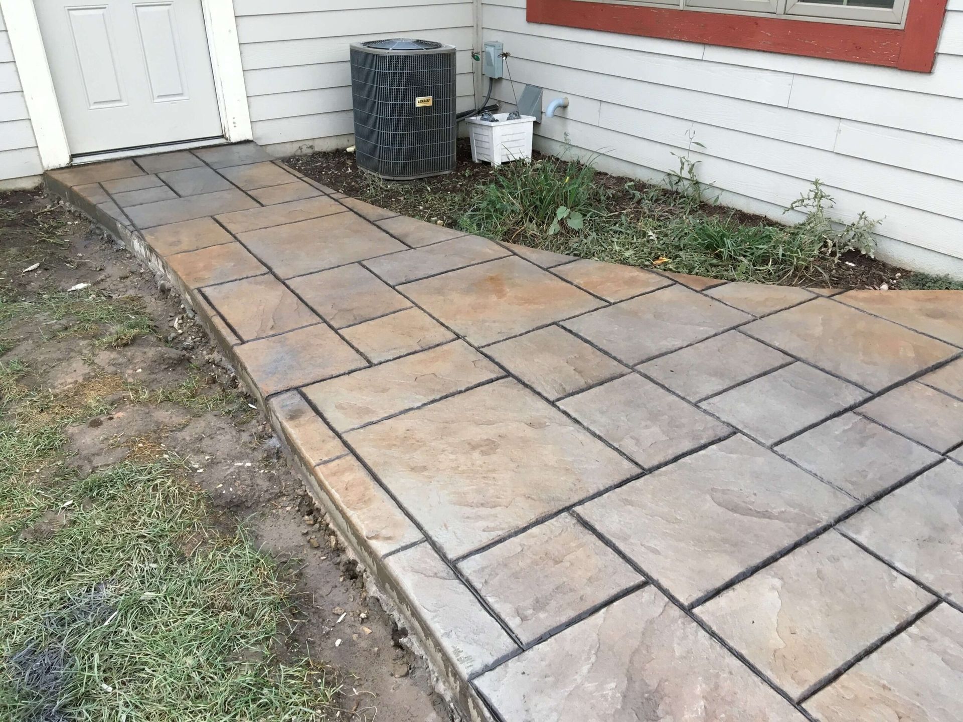 Stone paver walkway next to a building, leading to a door and air conditioning unit.