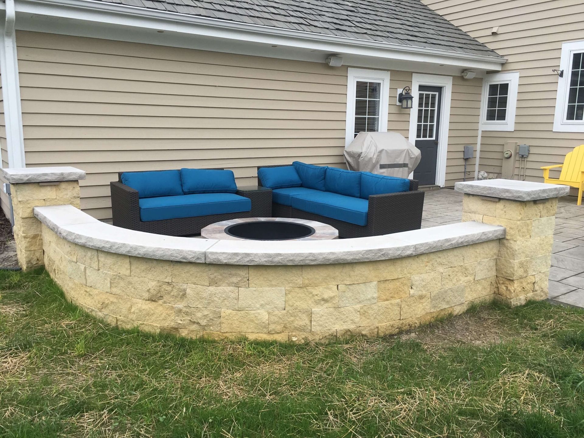 Outdoor patio with curved stone seating wall, sectional sofa, and fire pit.