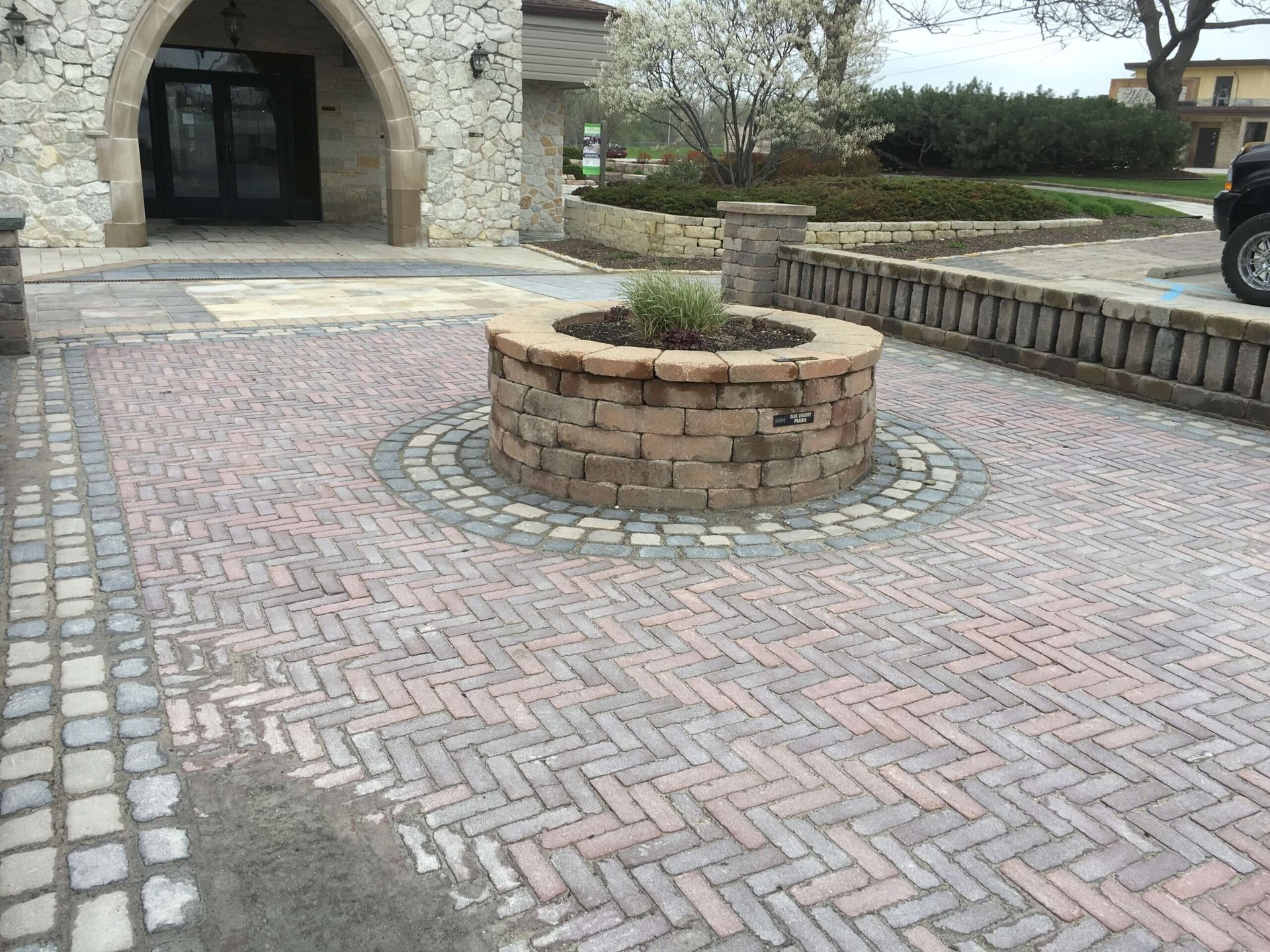 Brick patio with a circular planter and herringbone pattern leading to a building entrance.