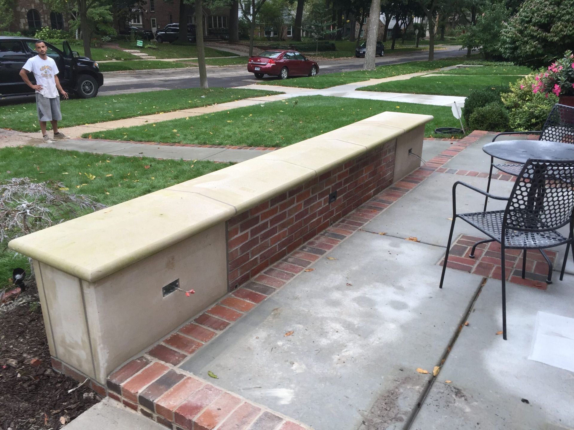 A low brick and stone wall with a person standing on a sidewalk. A car drives on a street nearby.