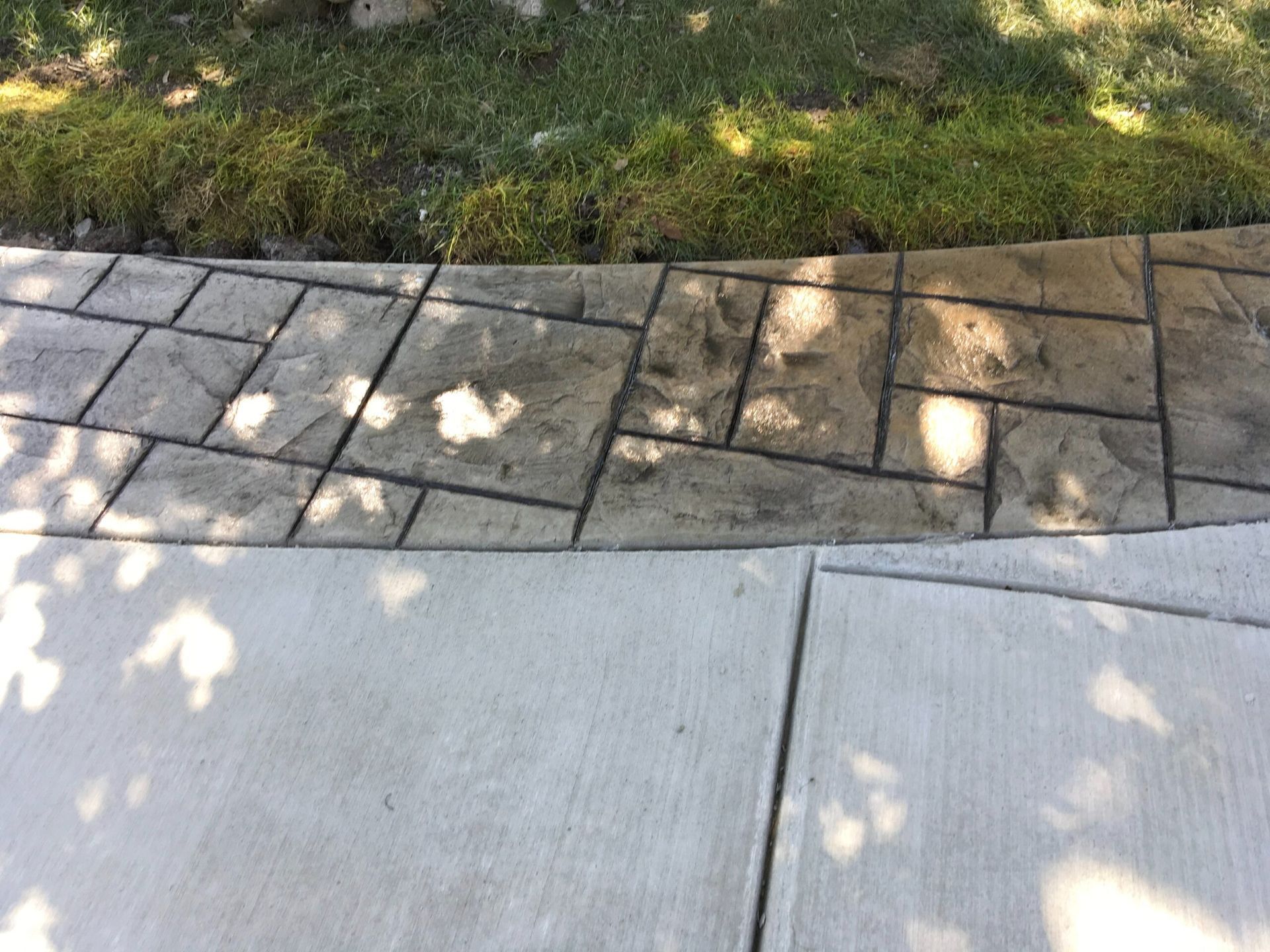 Concrete sidewalk alongside a textured, patterned concrete border with grass.
