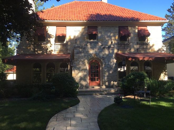 Stone house with red tile roof, arched doorway, and awnings, with a stone path leading to the entrance.