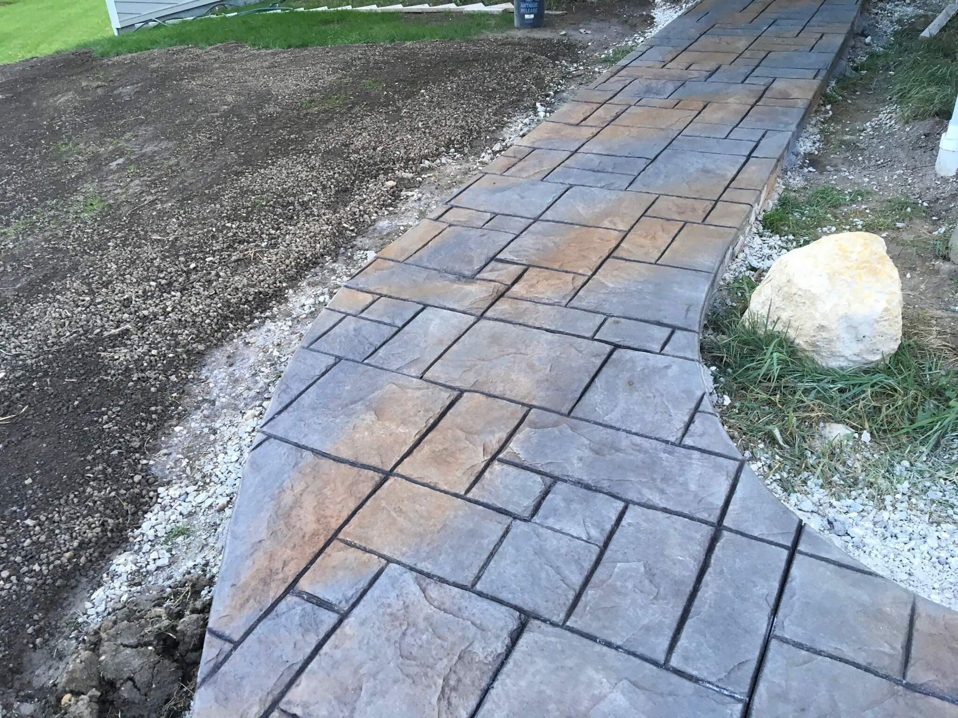 Concrete pathway with stamped stone pattern and color variations, curves through a grassy yard.