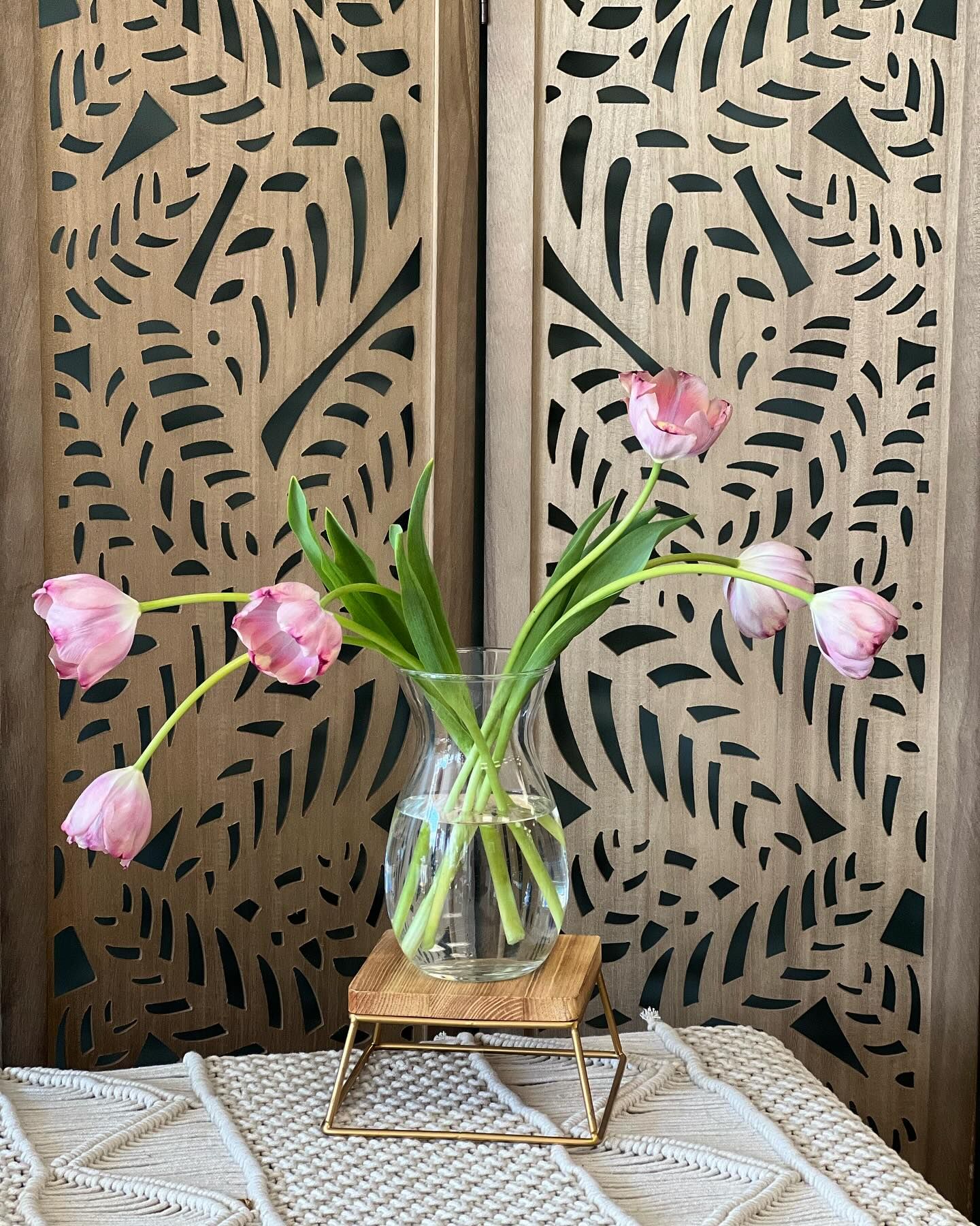 A vase filled with pink flowers is sitting on a table in front of a wooden screen.