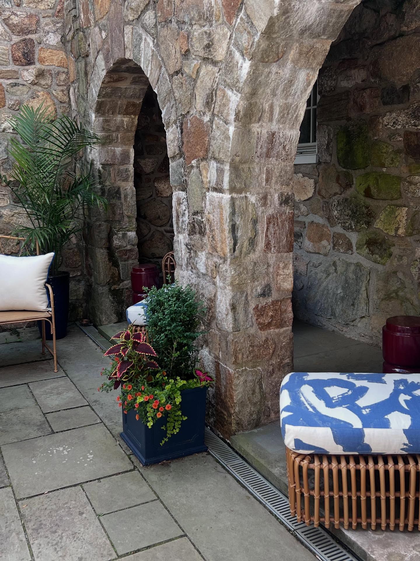A stone wall with arches and a patio with a chair and ottoman.