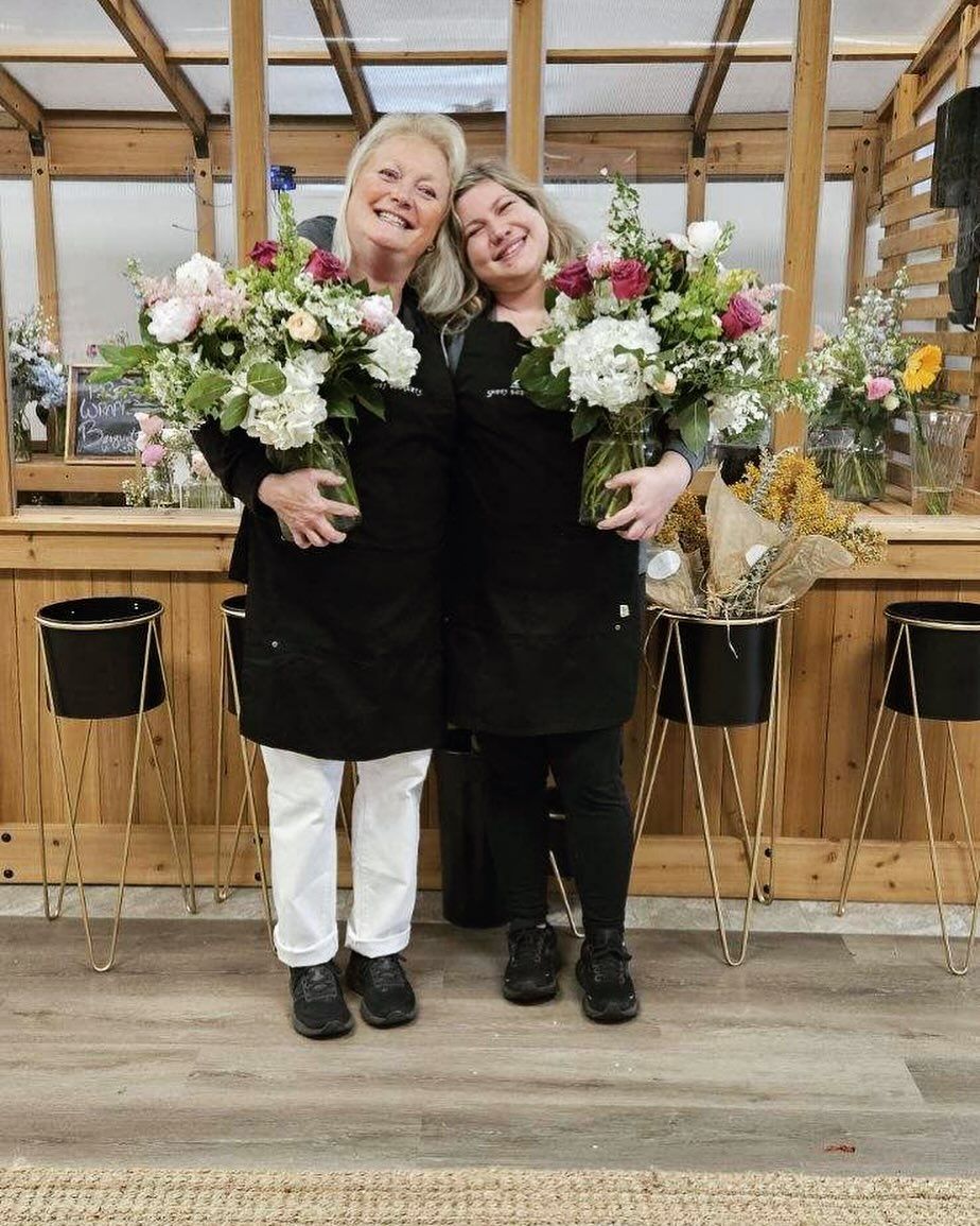 Two women are standing next to each other holding vases of flowers.