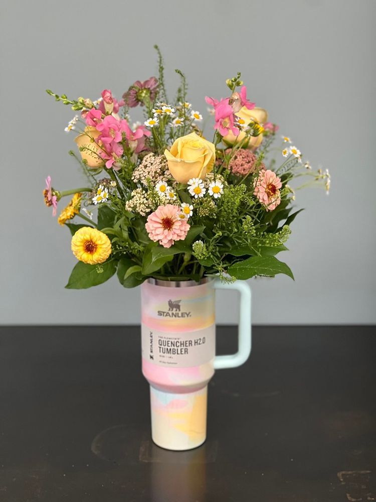 Colorful floral arrangement in a pastel Stanley tumbler, on a dark surface against a gray background.