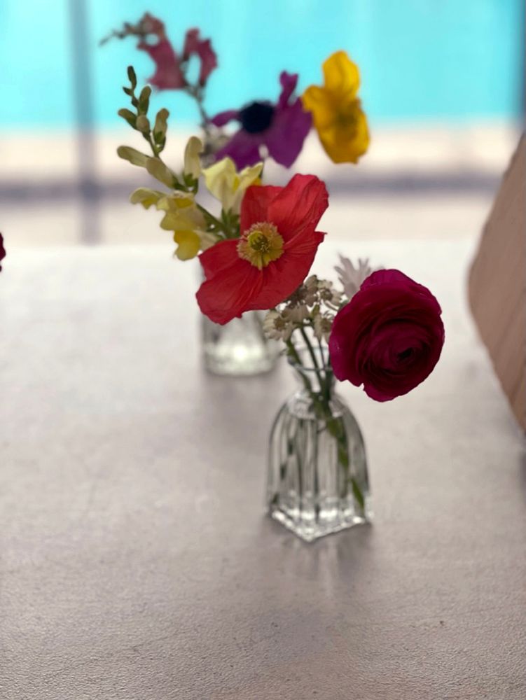 Small vases with colorful flowers on a white surface, blurred blue background.